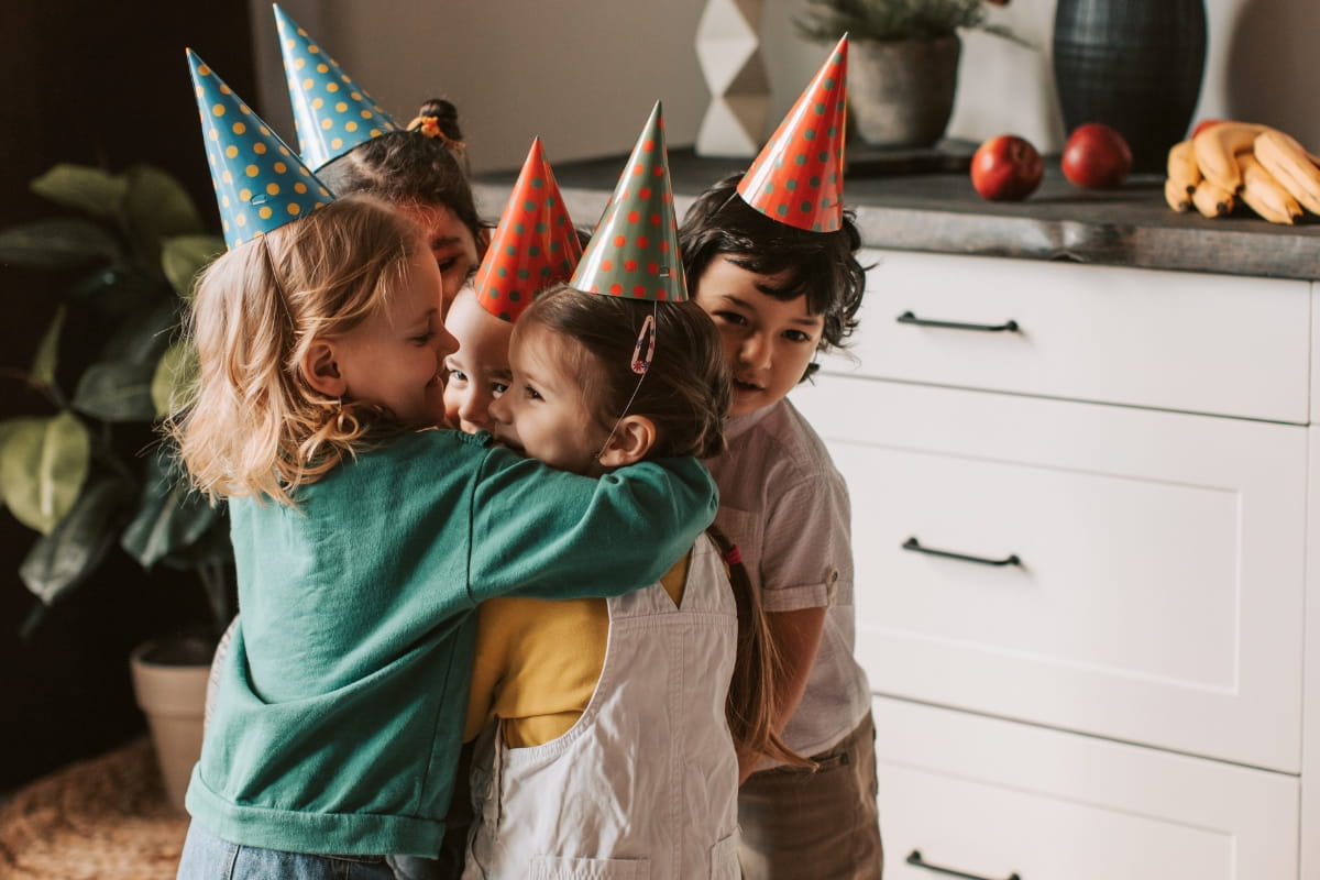 Kindergruppe mit Partyhütchen umarmt fröhlich ein Geburtstagskind – Geschenkideen für Kinder von 3 bis 7 Jahren