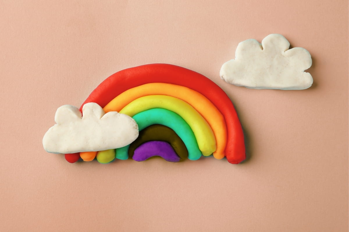 Regenbogen aus bunter Kinderknete auf cremefarbener Oberfläche – Sensory Play Idee für Kinder zuhause