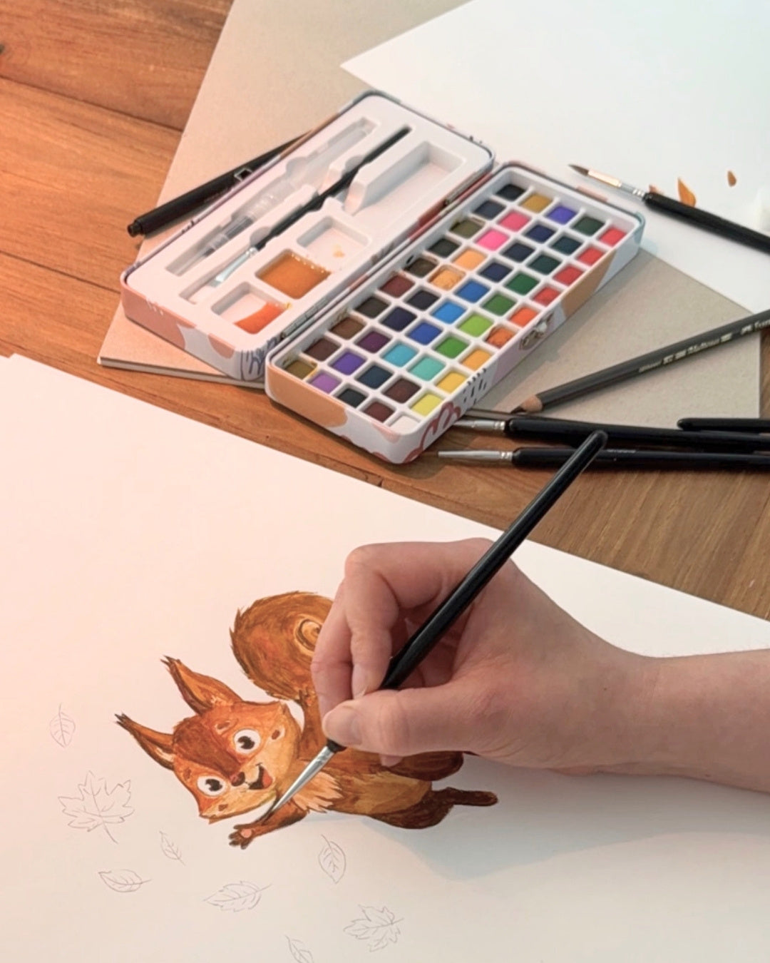 Hand mit Pinsel malt Aquarell-Skizze von Luni – Entstehung der Zendou Kids Illustration